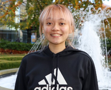 Female Asian student wearing a black hoody standing in front of a water fountain.